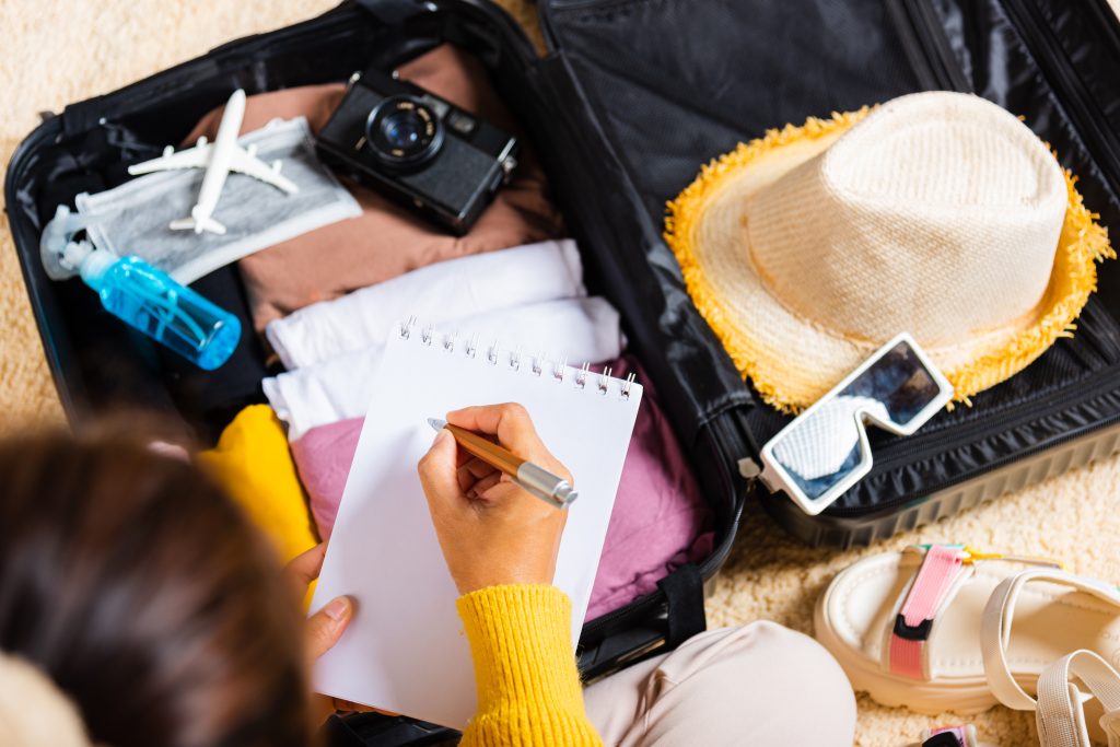 mujer escribiendo papel tome nota empacando maleta vacaciones escribiendo lista papel sentado habitacion